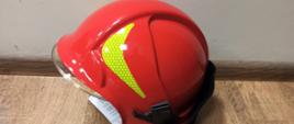 hełm strażacki koloru czerwonego z żółtym odblaskiem lezy na podłodze