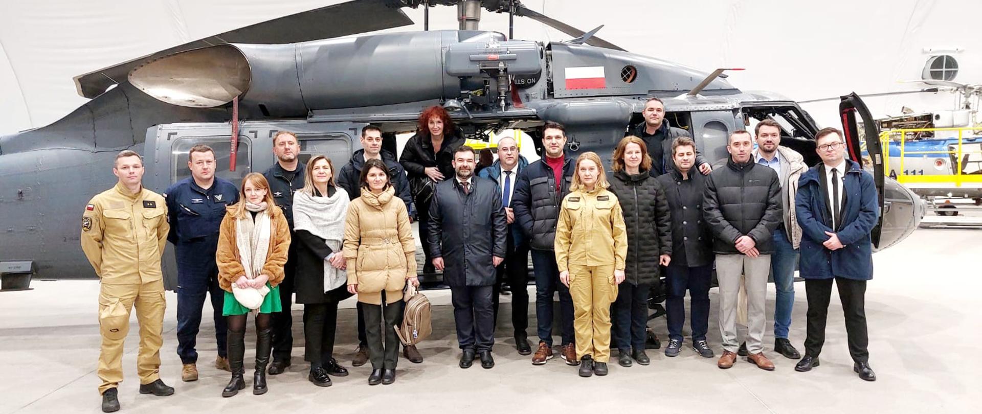 Delegacja ekspertów z Rumunii wraz osobami koordynującymi wizytę pozuje do zdjęcia pamiątkowego na tle śmigłowca