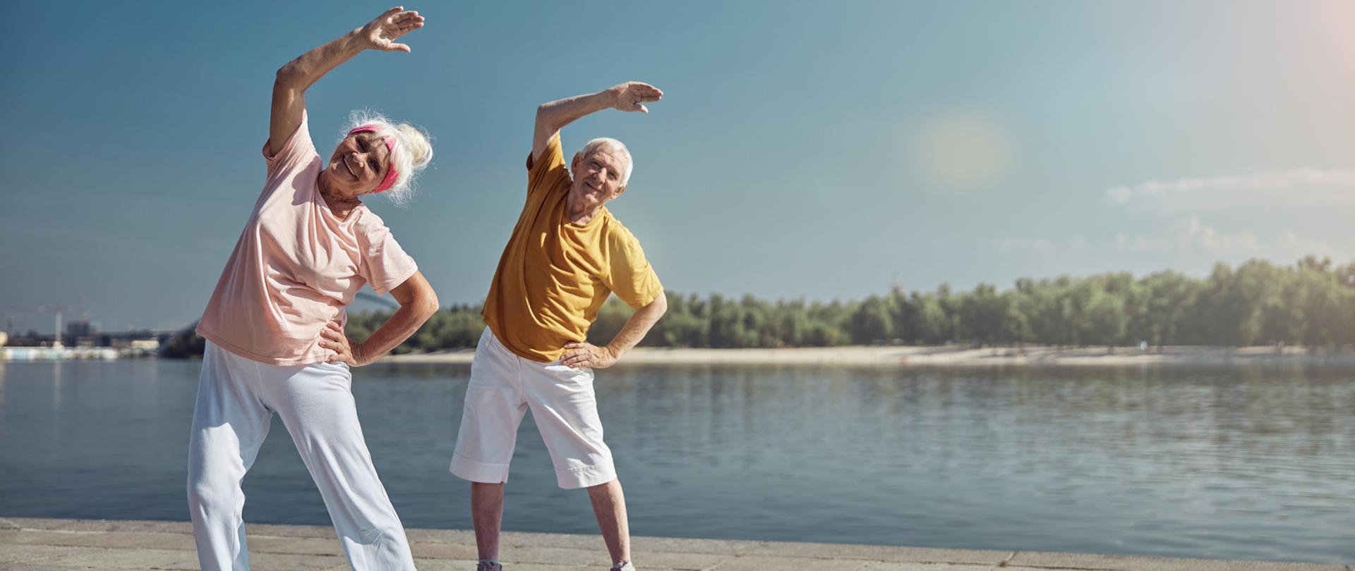 dwoje starszych ludzi gimnastykuje się nad brzegiem rzeki