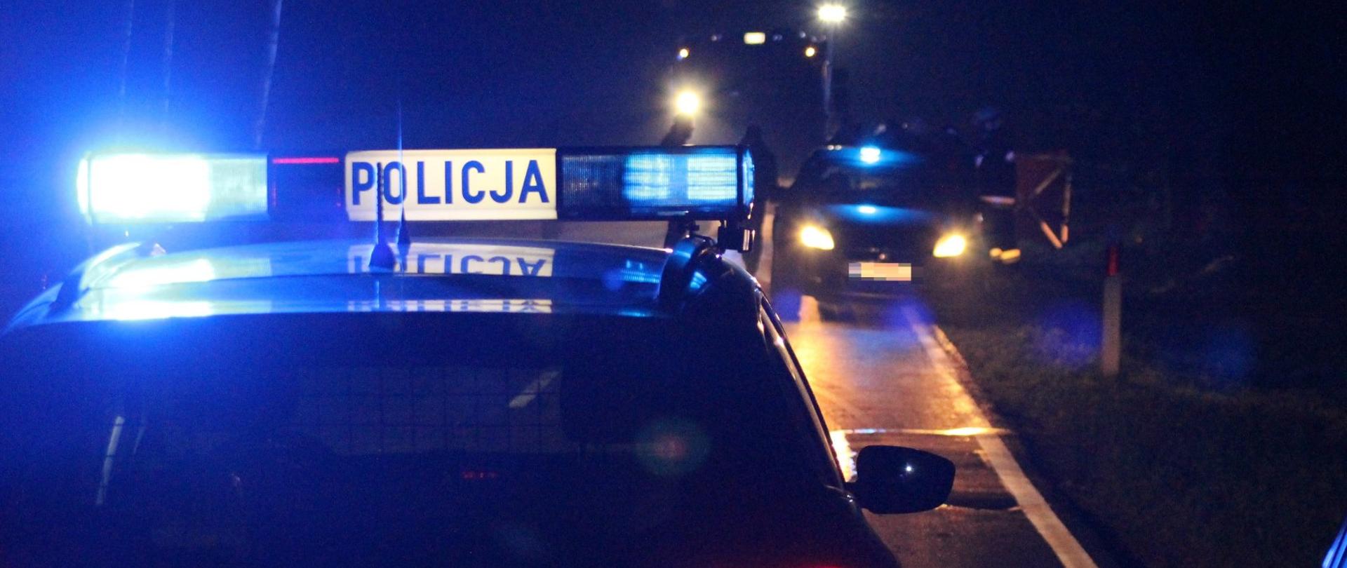 Pora nocna. Radiowóz policyjny z włączonymi światłami błyskowymi blokuje drogę. W oddali widać samochód pożarniczy. W miejscu w którym znajduje się potrącona kobieta policjanci prowadzą czynności dochodzeniowe. Teren ten wygrodzono parawanem ratowniczym.