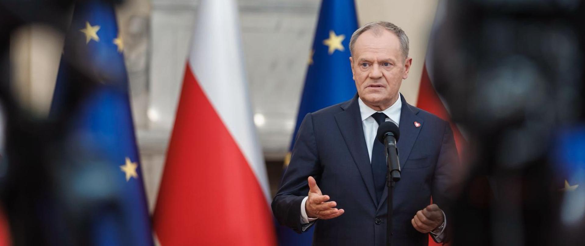 Premier Donald Tusk podczas konferencji prasowej w Sali Kominkowej KRPM, na tle flag Polski i Unii Europejskiej.