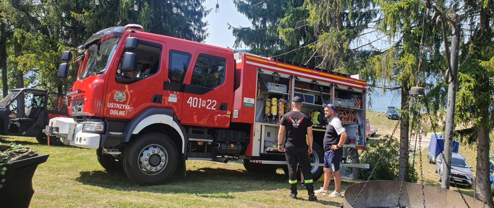 Zdjęcie przedstawia samochód średni ratowniczo-gaśniczy Renault D16 z otwartymi skrytkami. Przy samochodzie stoi strażak i rozmawia z mężczyzną.