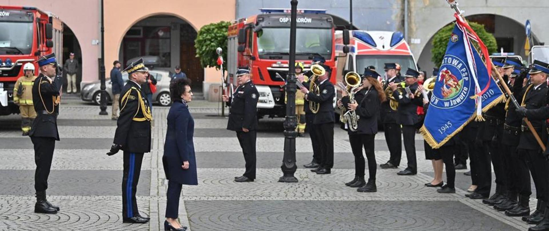 Przegląd pododdziałów w trakcie uroczystości. W tle samochody pożarnicze