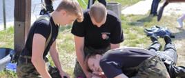 trzech chłopców wykonują czynności ratownicze polegające na sprawdzeniu tętna i oddechu u osoby wyjętej z rzeki