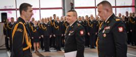 Komendant główny Państwowej Straży Pożarnej w towarzystwie odchodzącego i nowego podkarpackiego komendanta wojewódzkiego. W tle pododdział strażaków w umundurowaniu galowym. 
