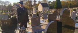 Na zdjęciu funkcjonariusz Państwowej Straży Pożarnej w mundurze wyjściowym stojący przed grobem zmarłego strażaka.