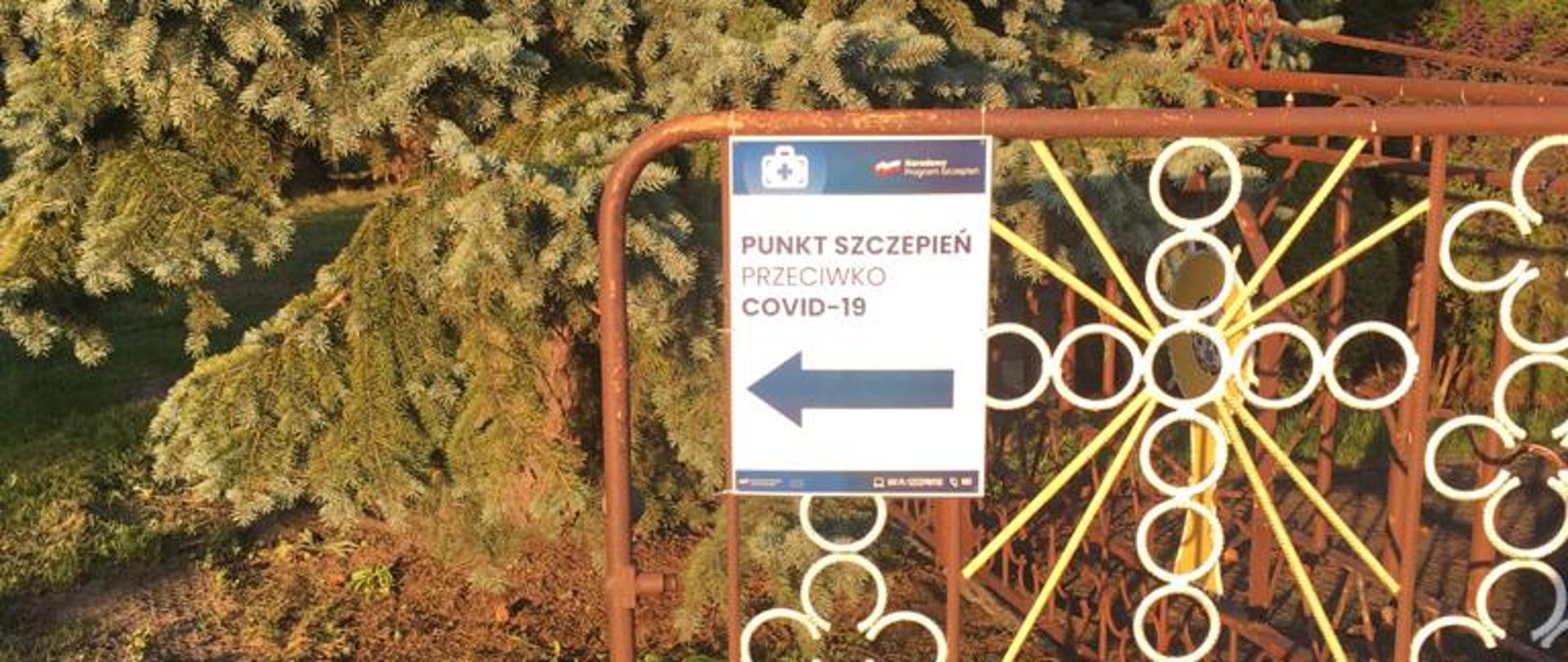 Na zdjęciu znajduje się brama , na której jest plakat z informacją, gdzie znajduje się punkt szczepień