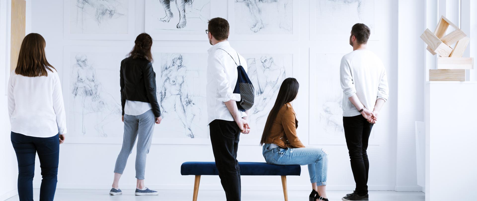 Grupa osób w muzeum ogląda szkice.