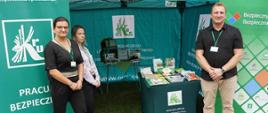 Zielony namiot promocyjny KRUS wyposażony w roll-upy i materiały promocyjne. Przed namiotem dwie kobiety i mężczyzna – pracownicy KRUS, uśmiechają się do zdjęcia.
