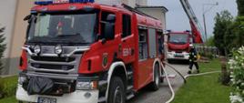 Samochód pożarniczy na pierwszym planie, w tle drabina mechaniczna z której strażak podaje wodę na dach kościoła