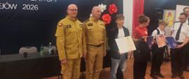 Na pierwszym planie uczestnicy turnieju, w rękach trzymają dyplomy, w centralnej części fotografii dwóch funkcjonariuszy PSP w żółtych ubraniach służbowych