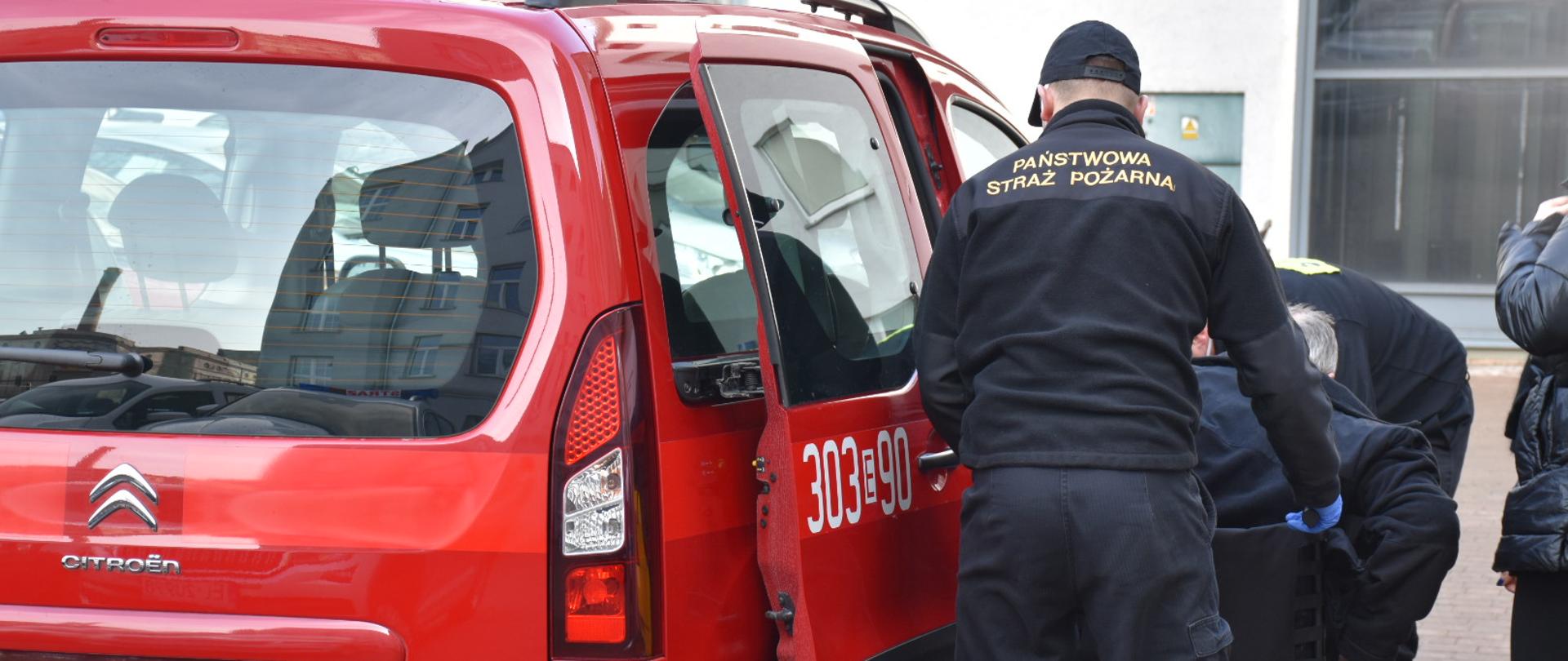 Na zdjęciu strażacy pomagający w transporcie osoby na szczepienie przeciw COVID-19