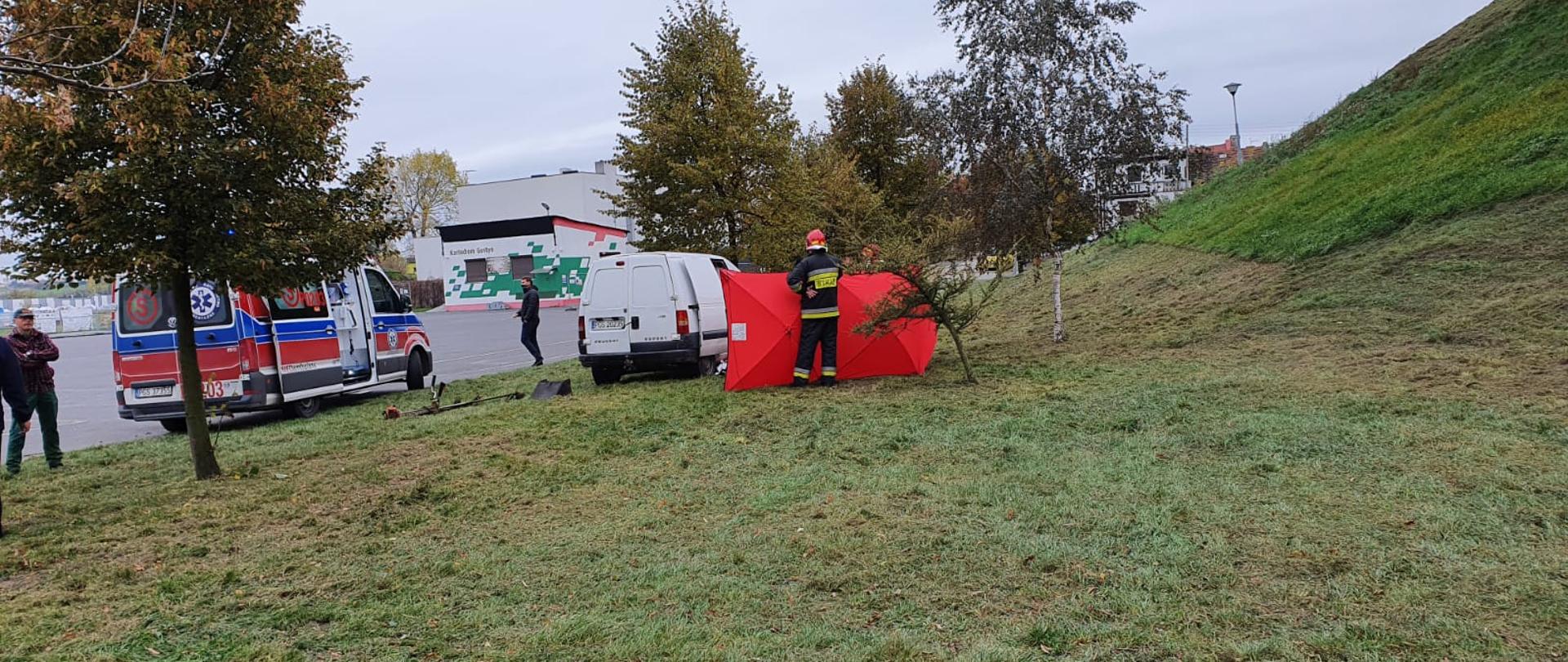 Zdjęcie przedstawia karetkę pogotowia, samochód strażacki oraz strażaków i ratowników udzielających pomocy. 