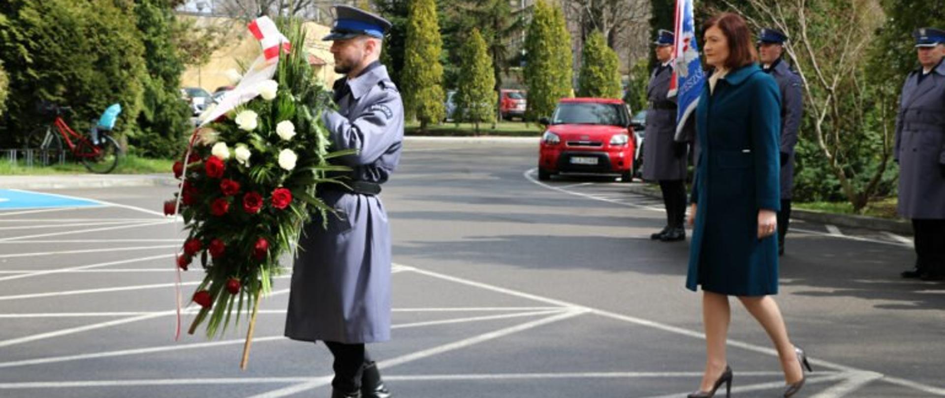 Wojewoda podkarpacki Ewa Leniart podczas składania wieńca pod tablicami memorialnymi na frontonie budynku Komendy Wojewódzkiej Policji w Rzeszowie. Przed wojewodą idzie policjant trzymający wiązankę kwiatów