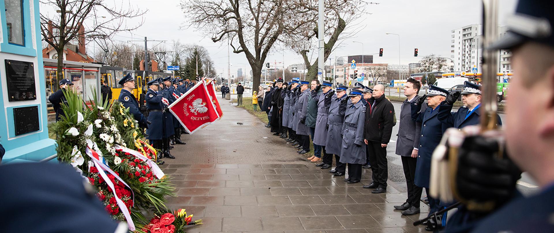 Na zdjęciu widać uczestników uroczystości stojących przed kapliczka na której znajduje się pamiątkowa tablica upamiętniająca śmierć podkom. Andrzeja Struja w momencie odgrywania melodii "Śpij kolego mój". Widać m.in dyrektora gabinetu politycznego Michała Prószyńskiego, gen. insp. Jarosława Szymczyka komendanta głównego Policji oraz nadinsp. Paweł Dobrodziej komendanta stołecznego Policji.