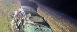 Zdjęcie w porze nocnej. Na zdjęciu uszkodzony pojazd. Zdjęcie na drodze publicznej. Oświetlenie sztuczne. W tle pole uprawne.