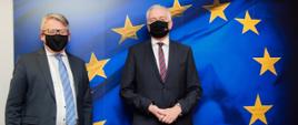 Wicepremier, minister rozwoju, pracy i technologii Jarosław Gowin w maseczce na twarzy, po jego prawej stronie stoi Komisarz ds. pracy Nicolas Schmit. Z tyłu flaga UE.
