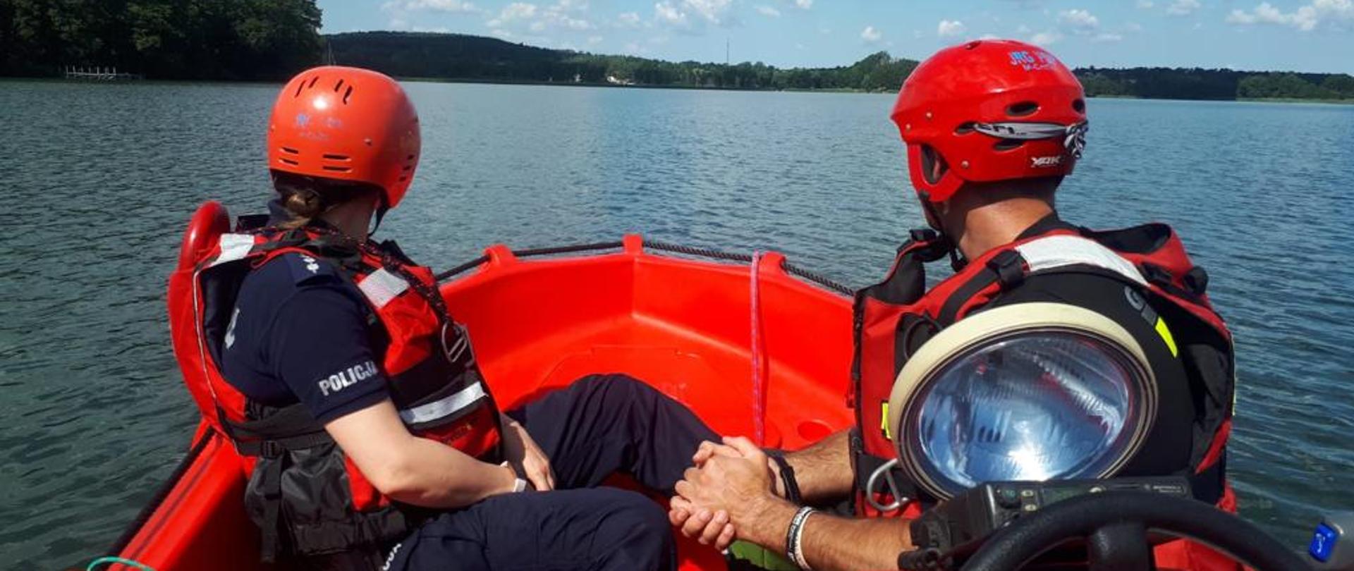Na zdjęciu widzimy strażaka oraz policjanta na łodzi. W tle widać jezioro.