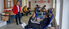 Na zajęciu widoczni mężczyźni i kobiety siedzący na fotelach na sali oddający krew podczas akcji zbiórki krwi zorganizowanej przez Klub Honorowych Dawców Krwi Polskiego Czerwonego Krzyża przy Komendzie Powiatowej Państwowej Straży Pożarnej w Gorlicach oraz personel z Regionalnego centrum Krwiodawstwa i Krwiolecznictwa.
