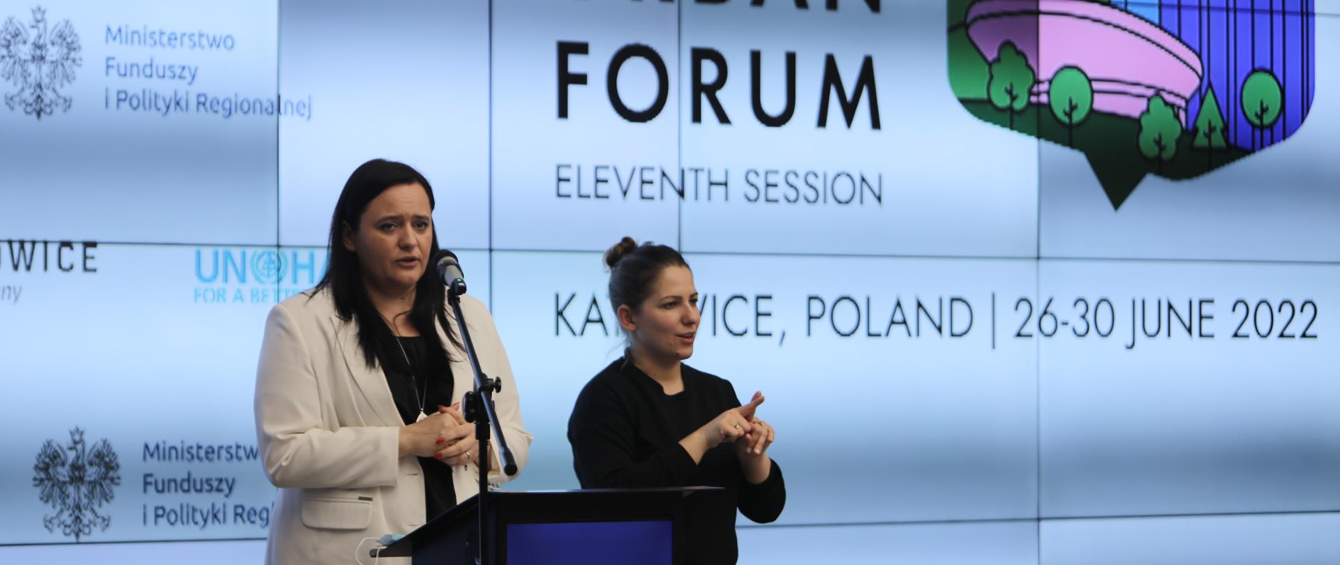 Na zdjęciu wiceminister Małgorzata Jarosińska-Jedynak w trakcie konferencji prasowej. Po prawej stronie tłumacz języka migowego. W tle ekran z logotypami Ministerstwa Funduszy i Polityki Regionalnej, UN-Habitat oraz Miasta Katowice.