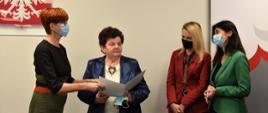 Za stołem konferencyjnym stoi europoseł Elżbieta Rafalska, dyrektor departamentu MRiPS Justyna Pawlak oraz dyrektor wydziału polityki społecznej LUW Grażyna Jelska. Wraz z nimi stoi wyróżniona uczestniczka 