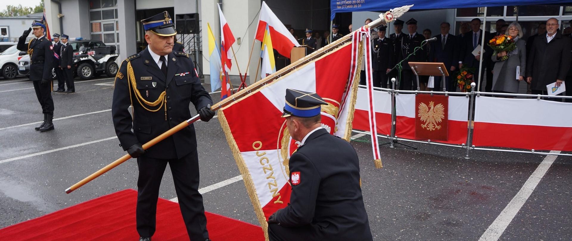 St. bryg. Arkadiusz Margoszczyn Komendant Miejski PSP w Opolu wita się ze sztandarem Komendy Miejskiej PSP w Opolu, trzymanym przez Opolskiego Komendanta Wojewódzkiego PSP w Opolu. W tle widoczni goście oraz strażacy PSP.