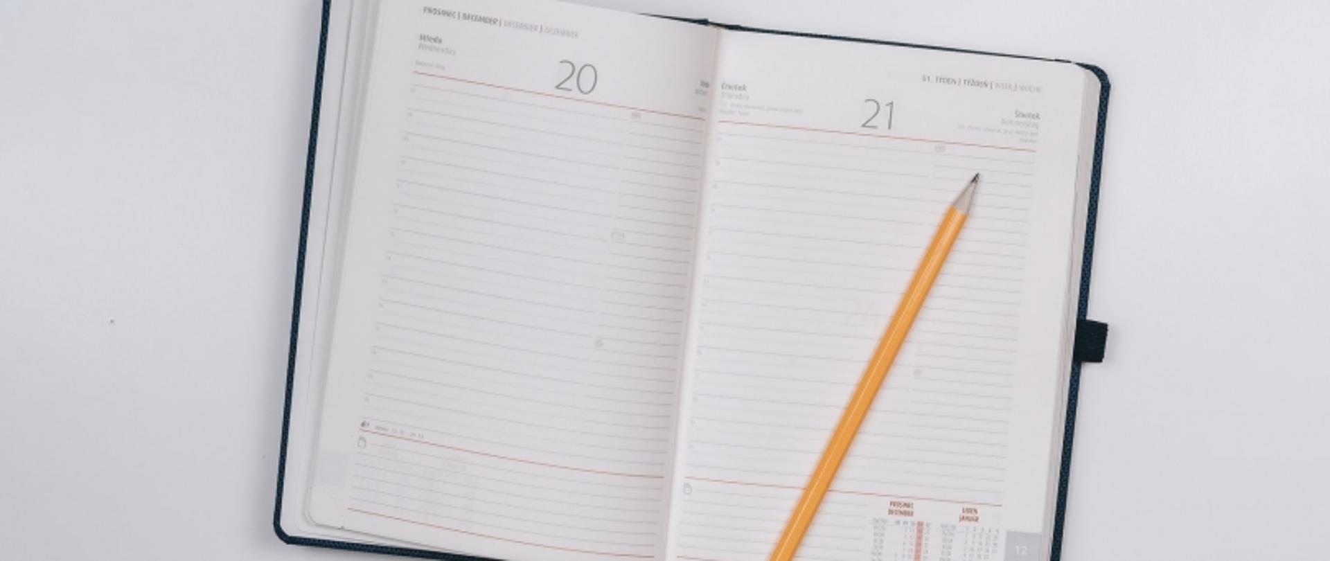 Otwarty planer z datami 20 i 21 oraz ołówkiem leżącym na stronie z napisem „WTOREK”.
