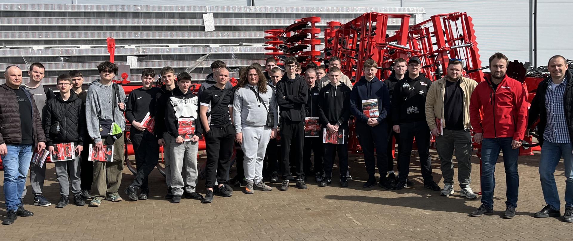 Zdjęcie grupowe uczestników wizyty studyjnej na tle maszyn rolniczych.