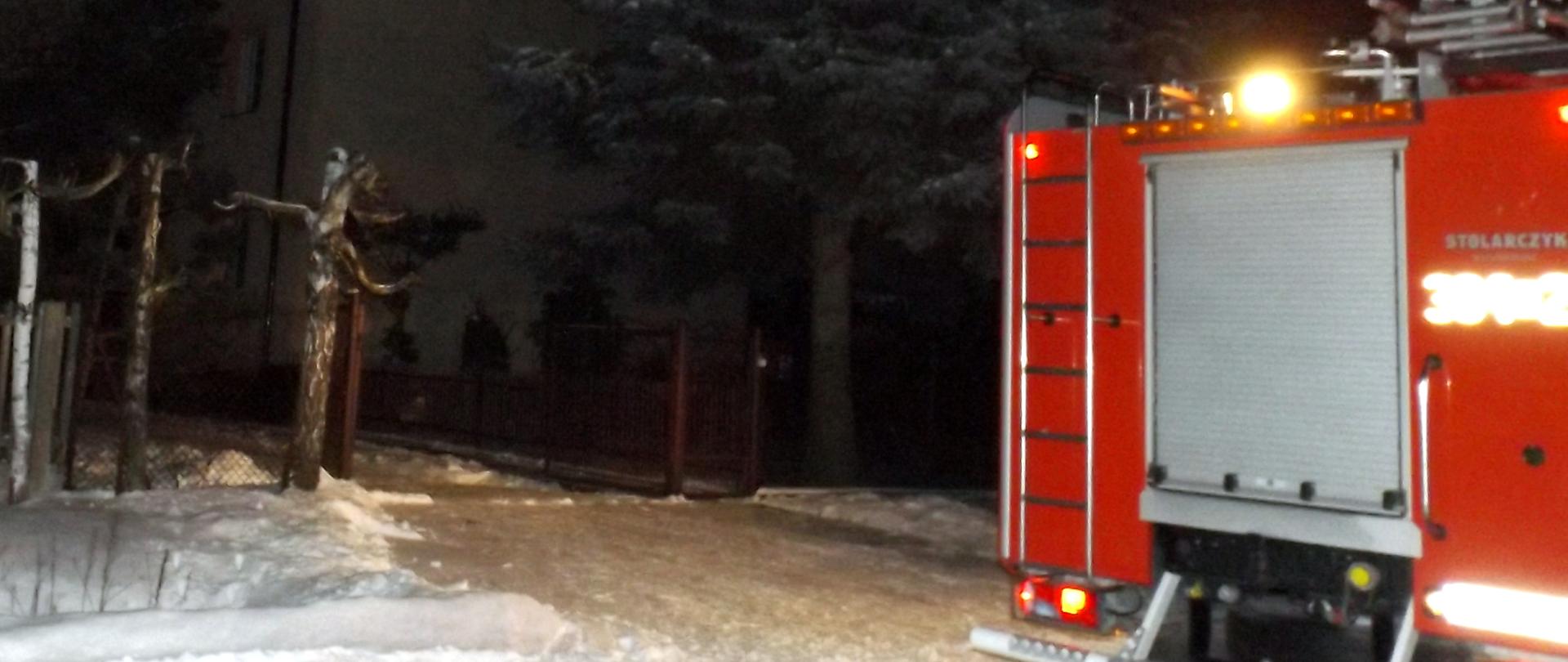Na zdjęciu znajduje się samochód pożarniczy, a tle dom w którym doszło do pożaru sadzy w kominie. Nie widać ognia ani dymu - jest wieczór.