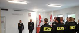 Strażacy podczas ślubowania, przed nimi komendant powiatowy PSP w Kolnie wraz z zastępcą dowódcy JRG, z boku stoi zmiana służbowa.