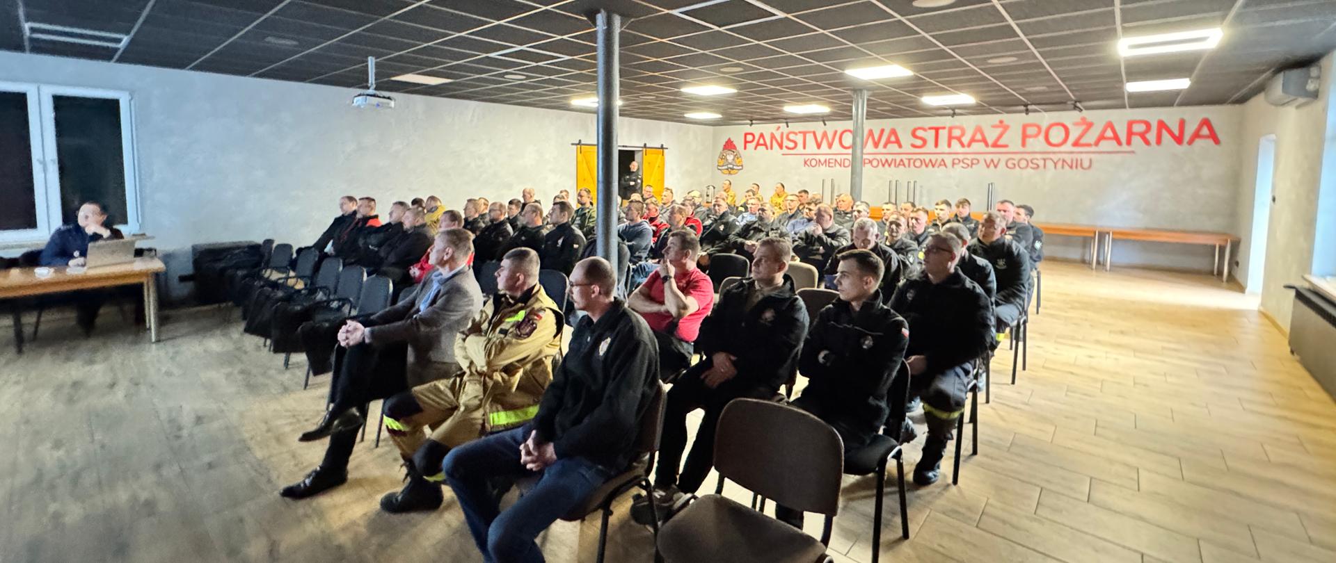 Uczestniczy siedzą w sali a wykładowca prowadzi zajęcia.