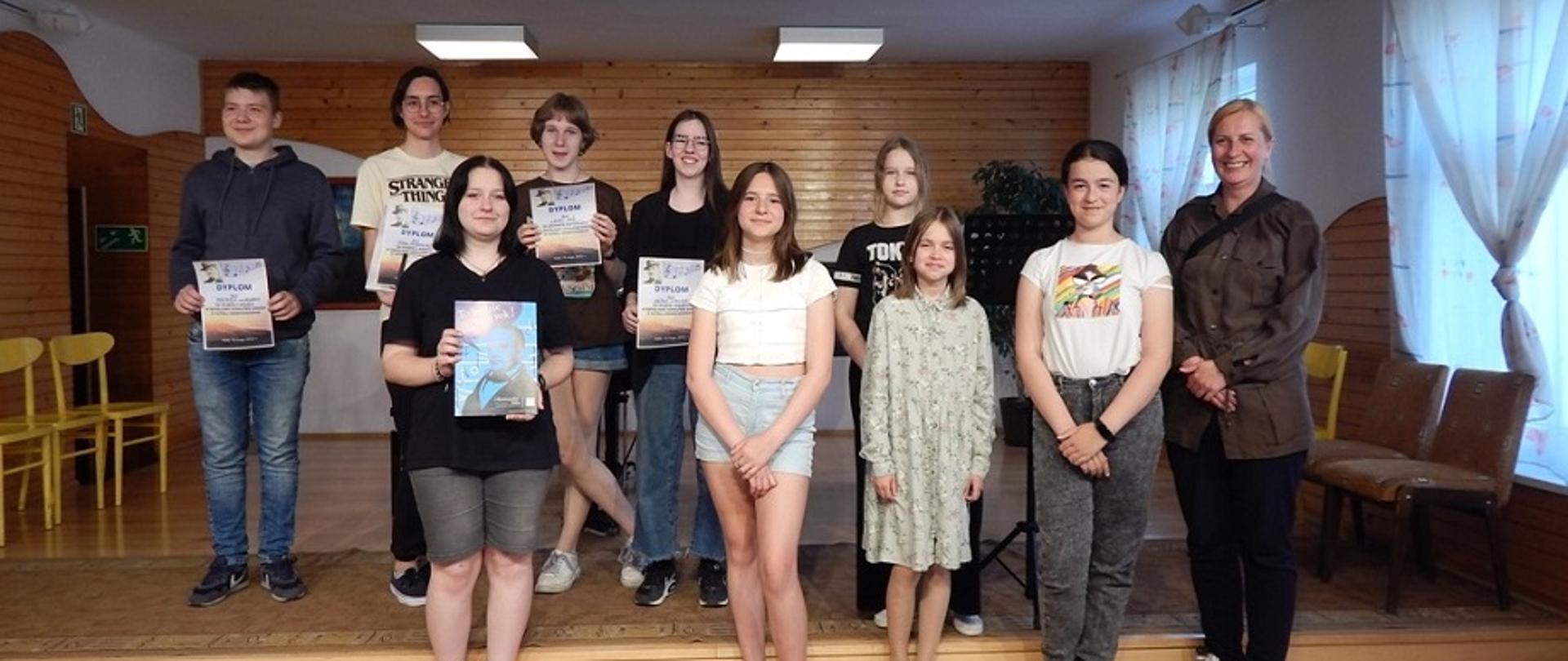 dzieci i młodzież wraz z opiekunem na scenie. Laureaci konkursu trzymają dyplomy.