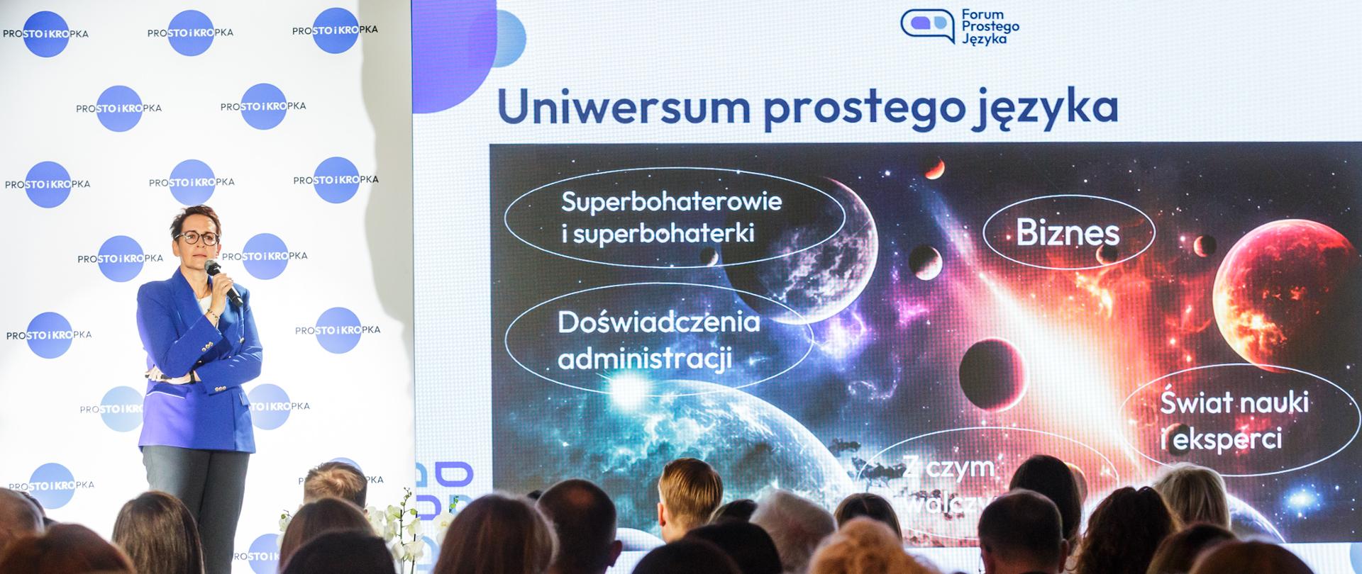 SSC na podium podczas prezentacji, w tle ekran z prezentacją