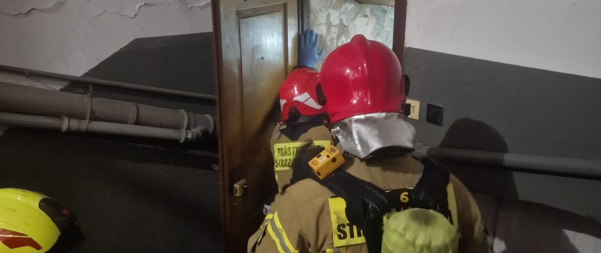 Strażacy w aparatach ochrony dróg oddechowych wchodzą do mieszkania.