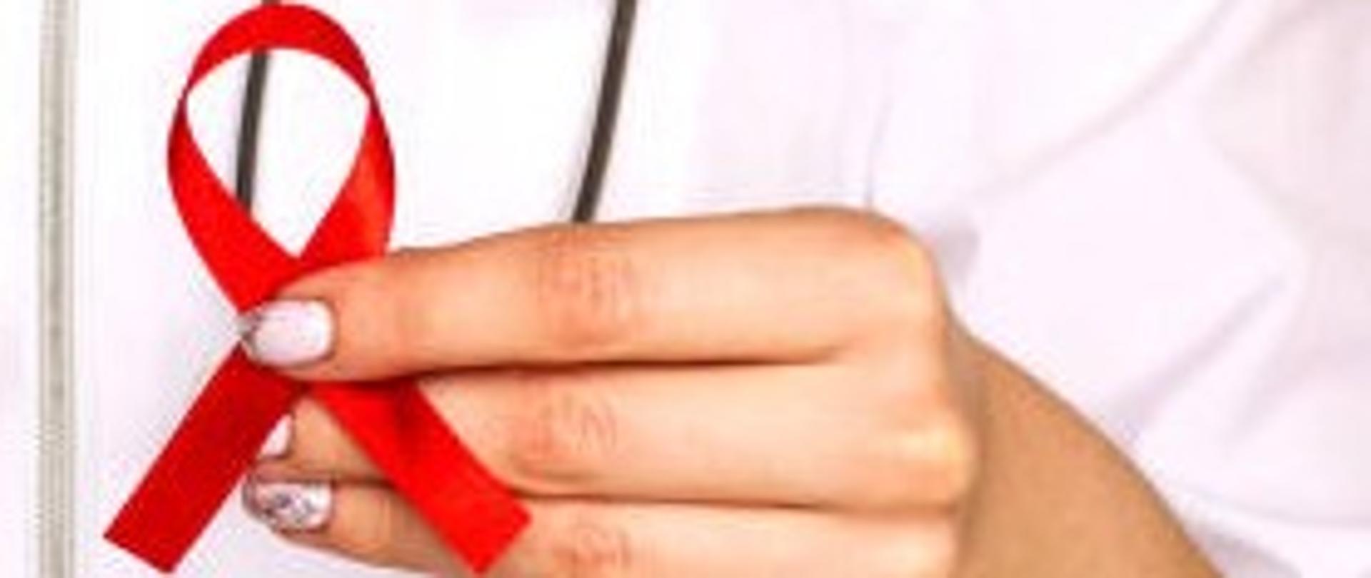 Zdjęcie przedstawia Czerwoną Kokardkę- symbol solidarności z osobami żyjącymi z HIV i chorymi na AIDS