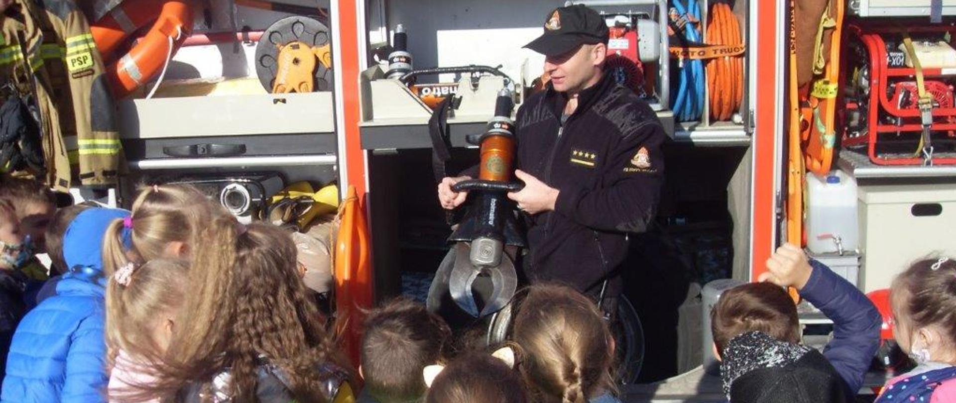 Zdjęcie przedstawia strażaka prowadzącego zajęcia z grupą dzieci