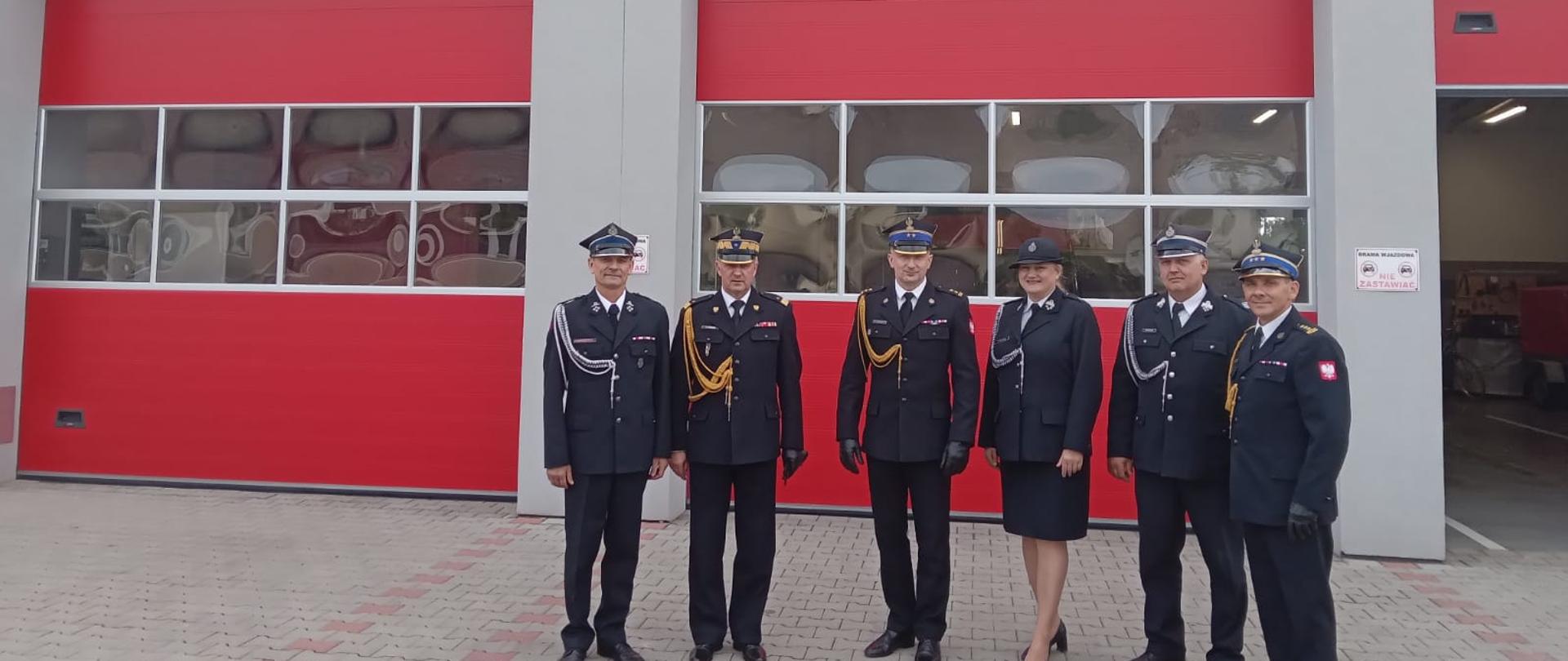 Strażacy stoją w rzędzie a w tle budynek i garażowy z czerwoną bramą. Na budynku napis OSP Kłodnica