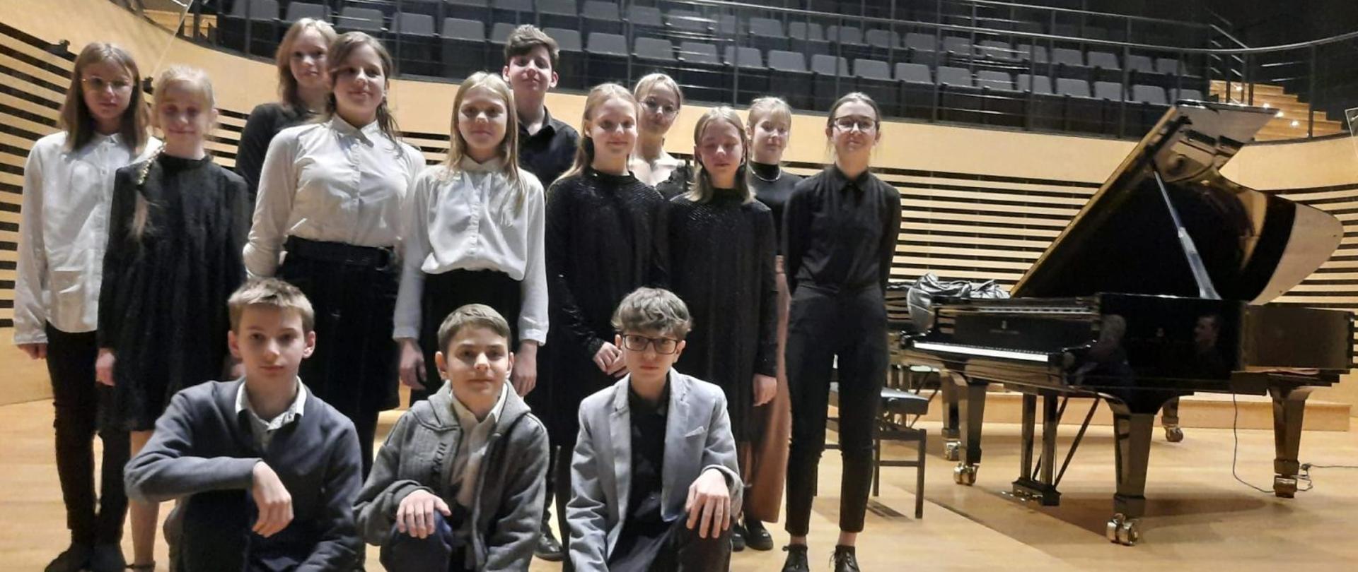 Zdjęcie przedstawia uczniów klasy fortepianu 14 osób w tle widać fortepian