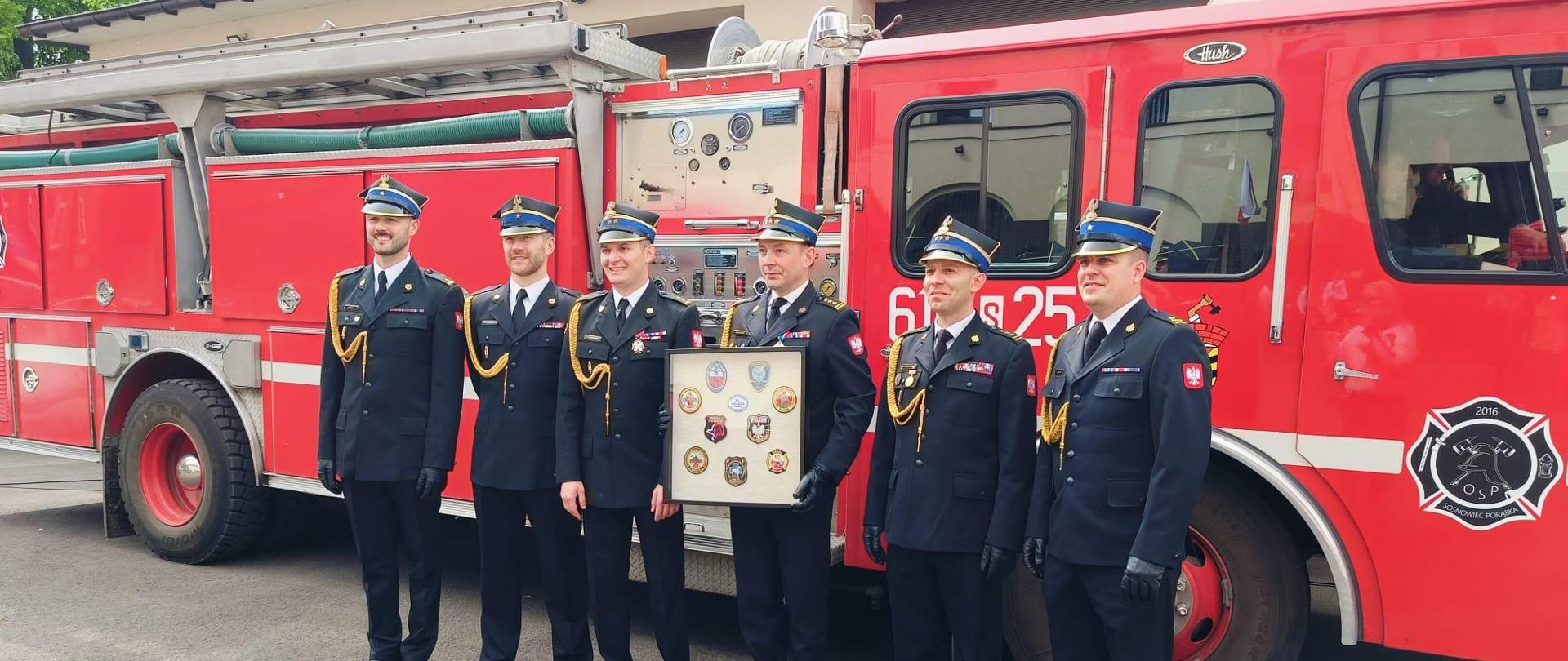 Pamiątkowe zdjęcie st. bryg. Jacka Szczypiorskiego na tle pojazdu pożarniczego w towarzystwie funkcjonariuszy PSP.