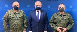 Wojewoda stoi na niebieskiej ściance promocyjnej Dowództwa Generalnego Rodzajów Sił Zbrojnych pomiędzy generałami Jarosławem Miką i Wiesławem Kukułą. Generałowie są ubrani w mundury, wszyscy mają na twarzach maseczki 