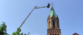 Zdjęcie przedstawia obiekt sakralny z wierzą oraz ramię podnośnika zbliżonego do szczytu wierzy.