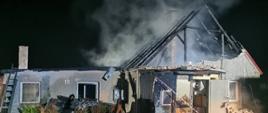 Budynek mieszkalny ze spalonym dachem, widoczne pozostałości konstrukcji dachowej nad którymi unoszą się kłęby dymu