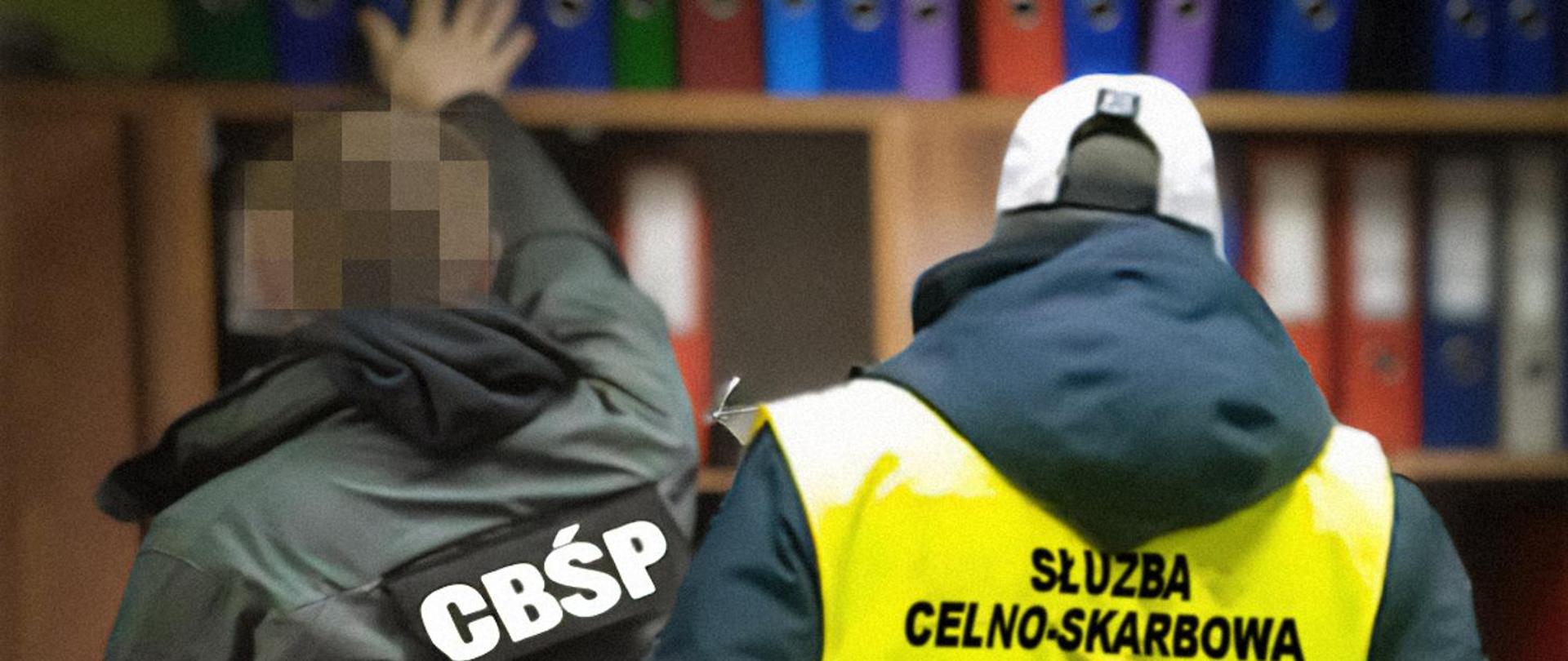 Funkcjonariusze CBŚP i Służby Celno-Skarbowej stoją przy regale z kolorowymi segregatorami.