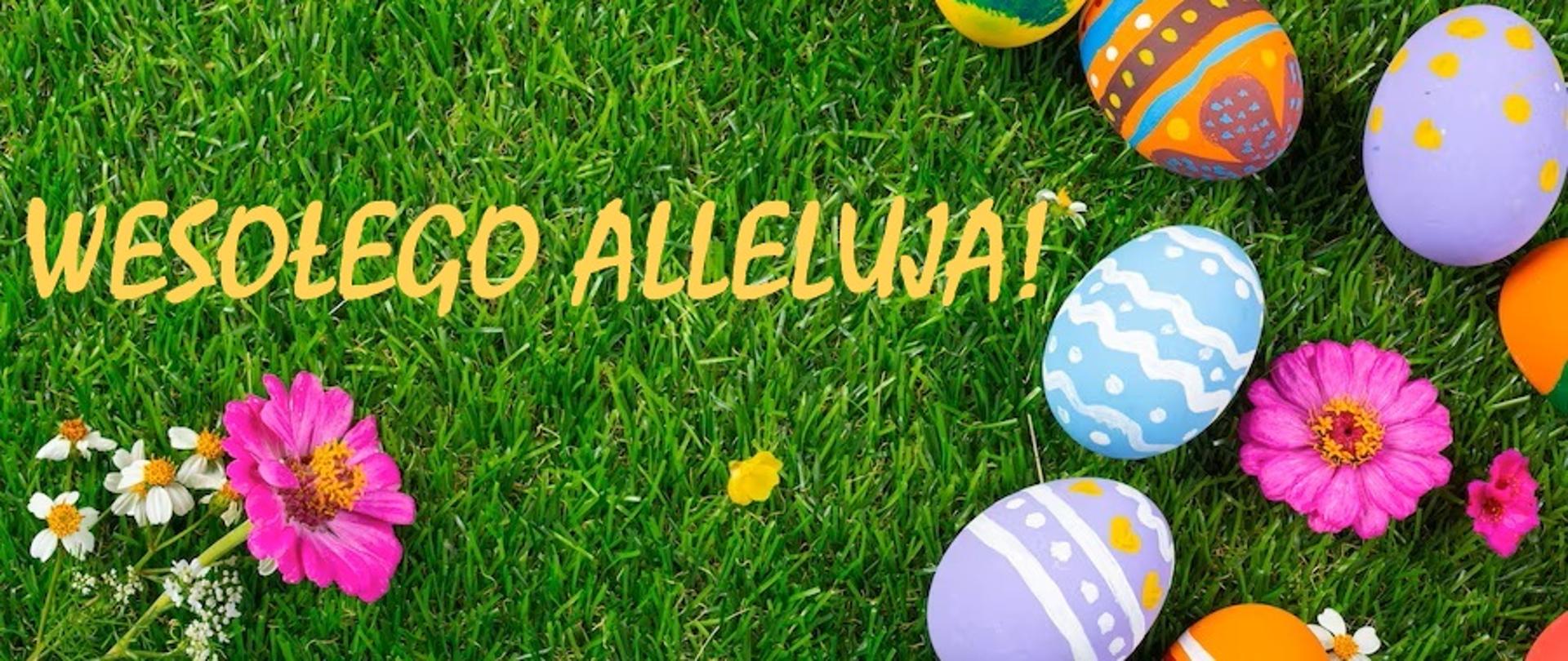 Na zielonej trawie po prawej stronie leżą pisanki. Po lewej stronie żółty napis Wesołego Alleluja!