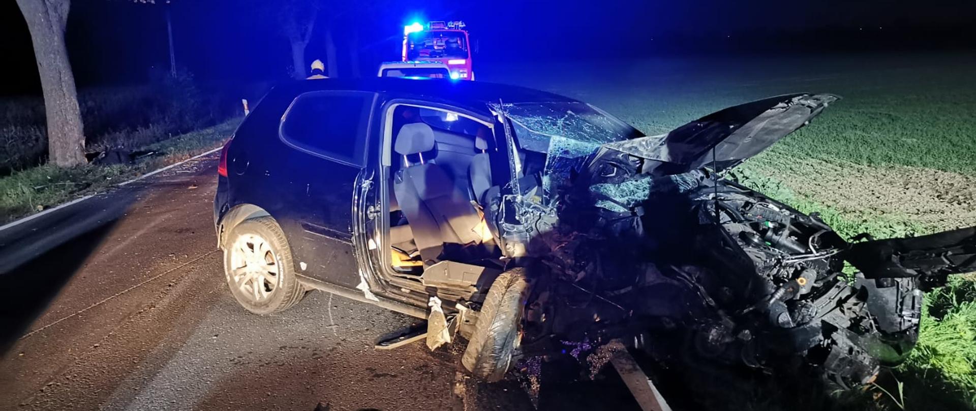 Na zdjęciu widać rozbite auto oraz strażaków i policjanta 