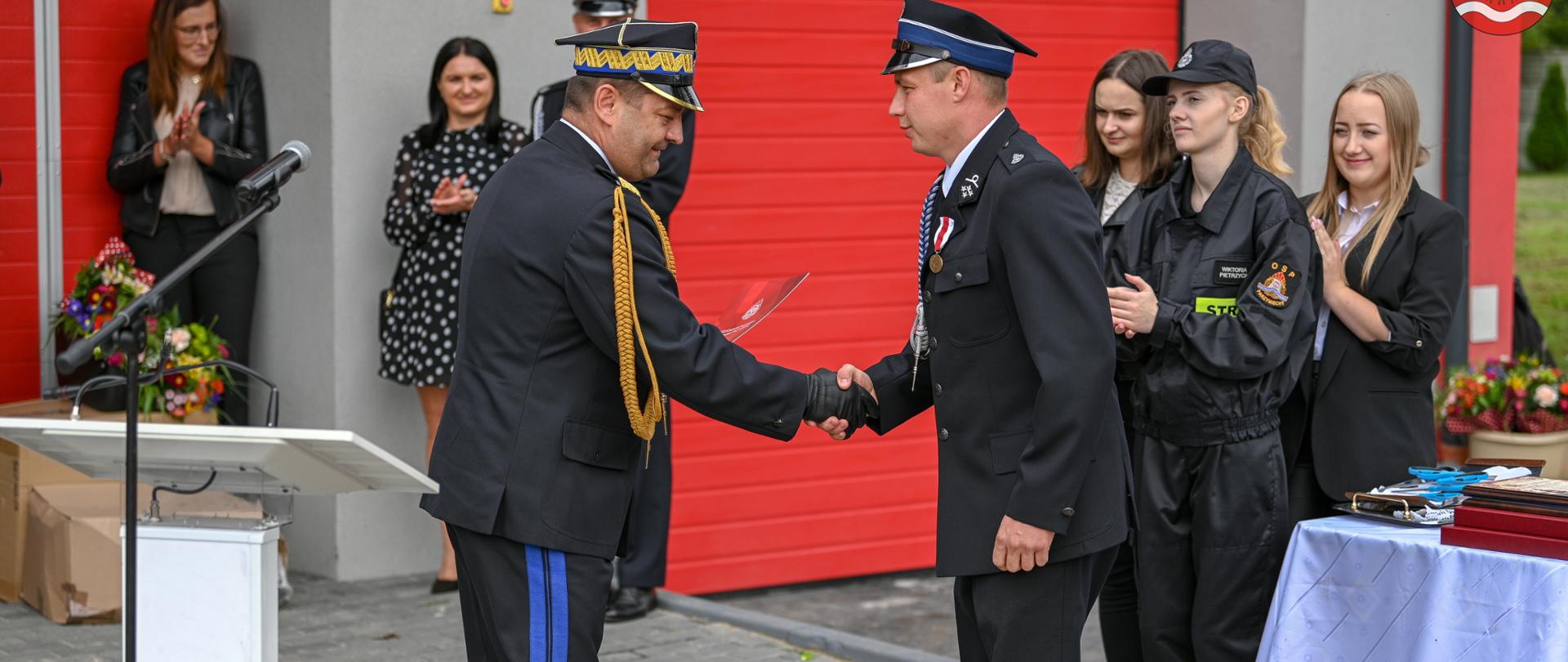 Zdjęcie przedstawia nadbrygadier Jacka Kleszczewskiego wręczającego dokumenty przekazania średniego samochodu ratowniczego druhowi Marcinowi Cieśli