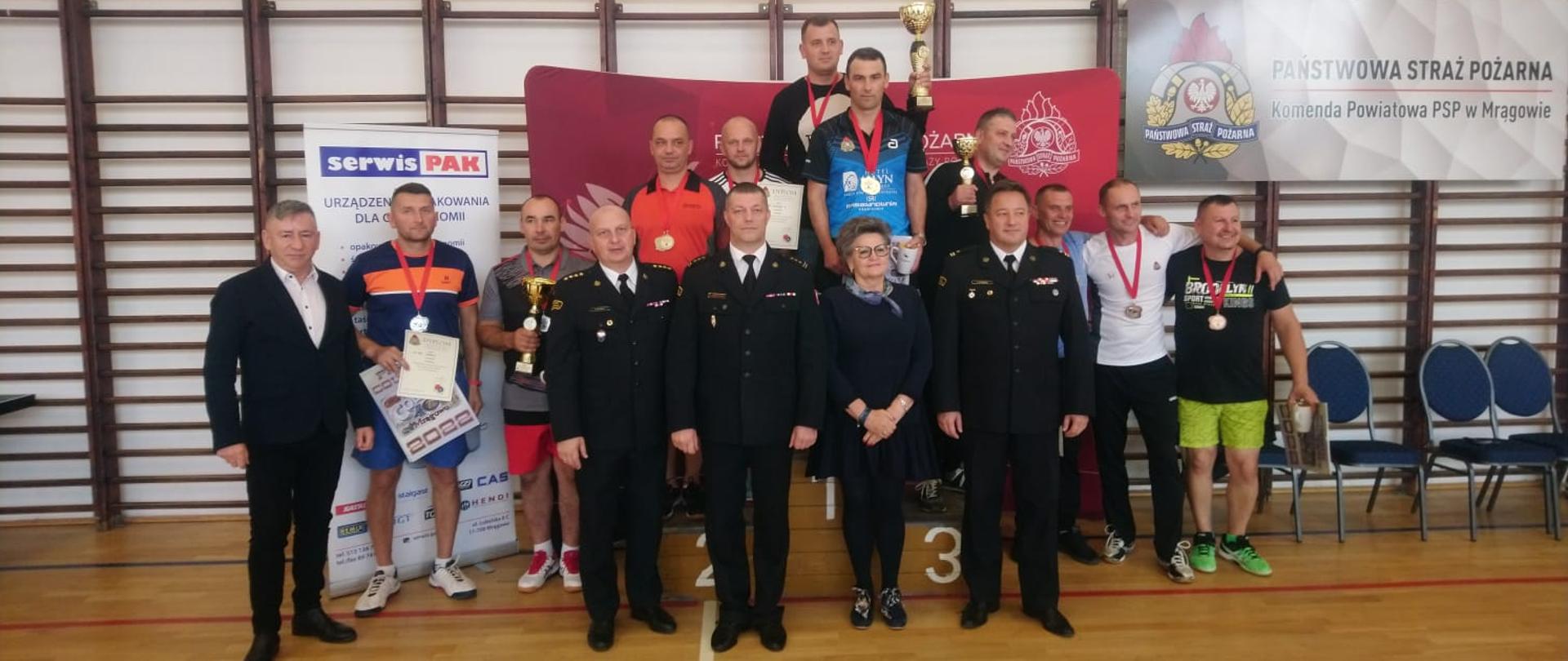 Zdjęcie grupowe zawodników biorących udział w turnieju. Strażacy stoją na podium.