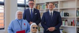Grupa czterech osób, na pierwszym planie dwie siostry zakonne, z odznaczeniami państwowymi (Krzyż Komandorski Orderu Odrodzenia Polski i Krzyż Oficerski Orderu Odrodzenia Polski), jedna z sióstr siedzi w fotelu inwalidzkim, na drugim planie stoi dwóch mężczyzn: Wicemarszałek Sejmu Szymon Hołownia oraz Podsekretarza Stanu Mateusz Kotecki; w tle regały z książkami i dwa zakratowane okna