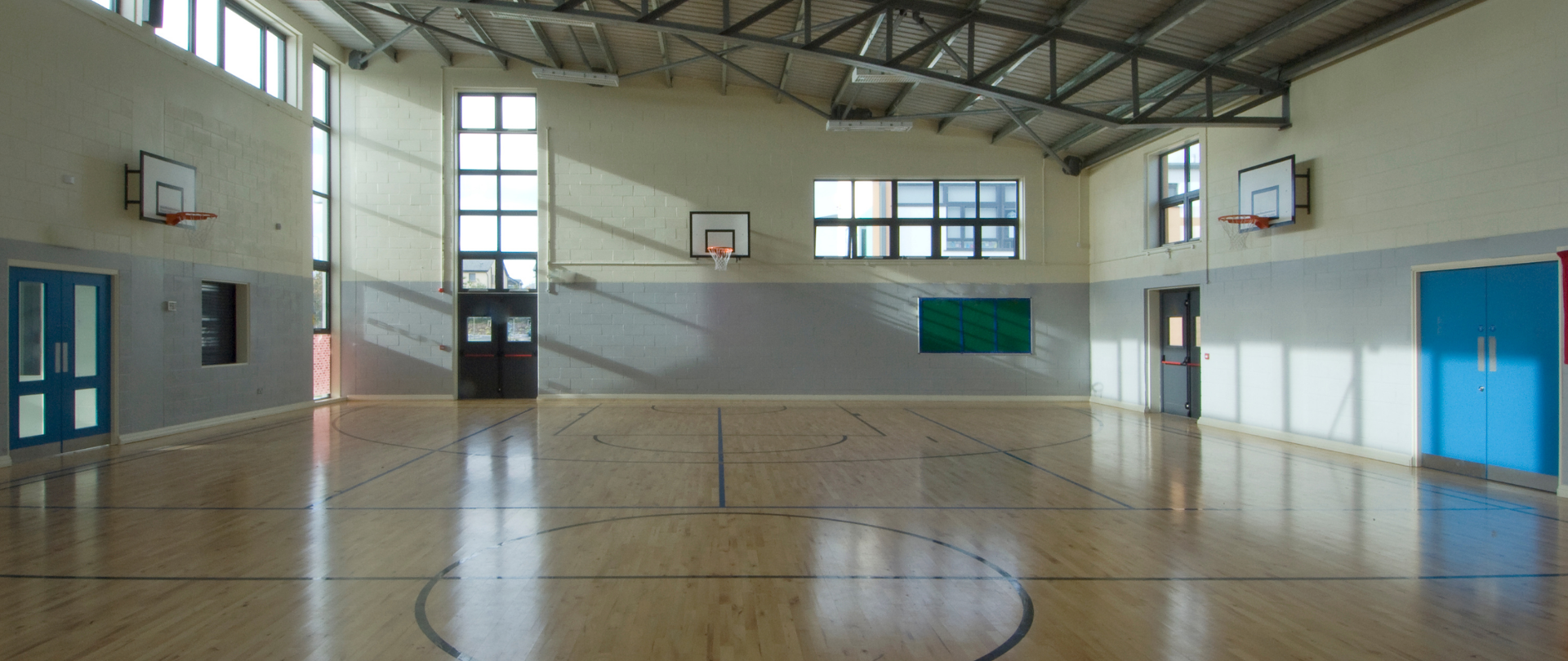 Zdjęcie sali gimnastycznej z narysowanymi liniami do gry w koszykówkę oraz z koszami do gry w koszykówki.