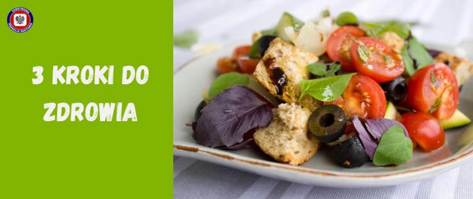 Z prawej strony na szarym obrusie w pasy stoi biały talerz ze złotym rantem na którym znajduje się sałatka warzywna składająca się z pokrojonych czerwonych pomidorów, czarnych oliwek, liści bazylii, sałaty i kawałków pełnoziarnistych grzanek. Po lewej stronie na zielonym polu beżowy napis 3 kroki do zdrowia. W lewym górnym rogu logo Państwowej Inspekcji Sanitarnej.